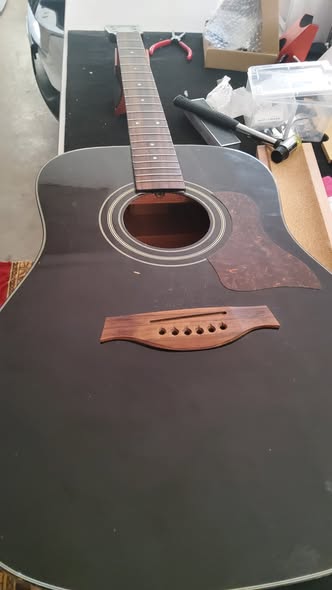 Black Travis acoustic on the workbench with strings and bridge saddle removed, top prepped for crack repair